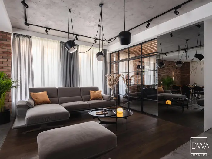 Industrialny salon z cegłą, szarą sofą i biurem za szklaną ścianką - dom pod Krakowem