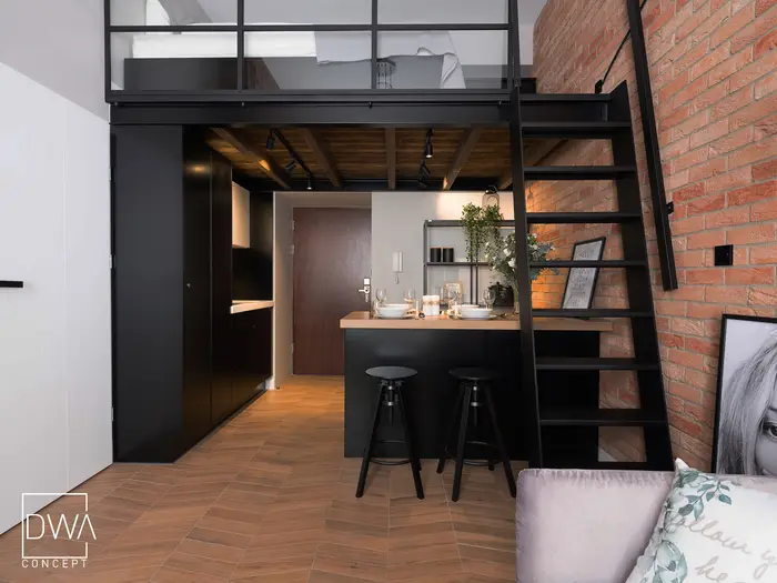 Wnętrze studio z antresolą sypialnianą, czarną drabinką i kuchnią w zabudowie - apartament w Krakowie 22m2