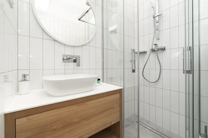 Łazienka z owalną umywalką na drewnianej szafce i prysznicem w białych płytkach - apartament w Krakowie 22m2
