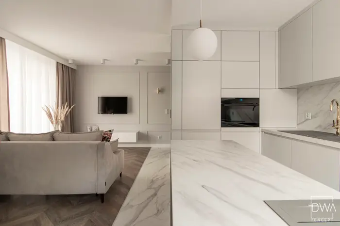 Kuchnia z białą zabudową, marmurową wyspą i lampami wiszącymi - apartament 46m2 w Krakowie